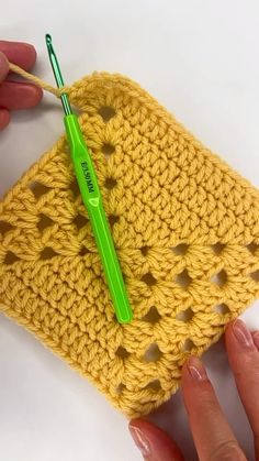 a crocheted square with a green pen sticking out of the middle, being held by someone's hand