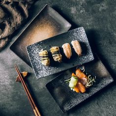 two black plates with sushi and chopsticks on them