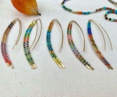 five pairs of colorful beaded hair pins on a white surface next to an orange leaf