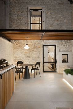 an open kitchen and dining area in a stone walled building with exposed ceilings, wood beams, and black chairs