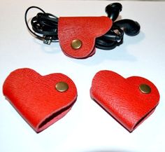 two heart shaped red leather cases sitting on top of a white table next to headphones