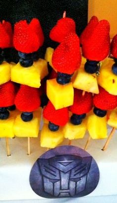 some strawberries and pineapples are arranged in the shape of robot suits on sticks