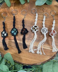 five tasselled keychains on a wooden board with green leaves in the background