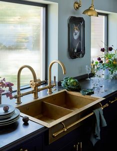 a kitchen sink with two faucets in front of it and flowers on the counter