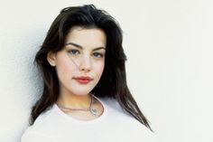 a woman wearing a white shirt is leaning against a wall and looking at the camera