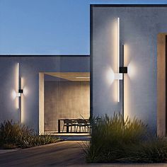 the exterior of a modern house with lights on it's side and an outside dining area