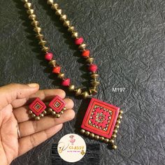 a hand holding a red and gold beaded necklace with matching earrings on top of it