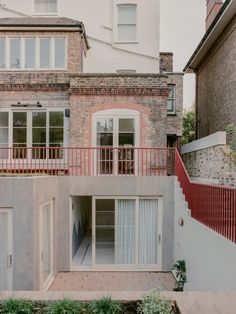 an apartment building with red railings and white doors on the second floor, surrounded by brick buildings