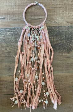 a pink necklace with beads and tassels hanging on a wooden wall next to a piece of wood