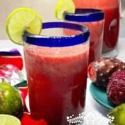 two glasses filled with fruit and juice next to limes