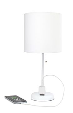 a white table lamp sitting next to a remote control and a cell phone on top of it