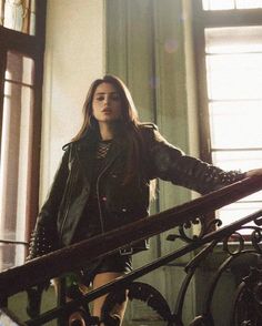 a woman is walking down the stairs in a black leather jacket and skirt with laces