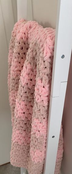 a crocheted blanket hanging from the side of a white door with pink and beige colors