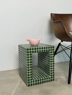 a chair next to a table with a bird on it and a small vase sitting on top of it