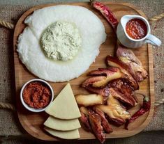 a wooden plate topped with meat, cheese and sauces next to other food items