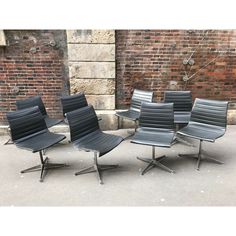 four black leather office chairs sitting in front of a brick wall, with one chair facing the camera