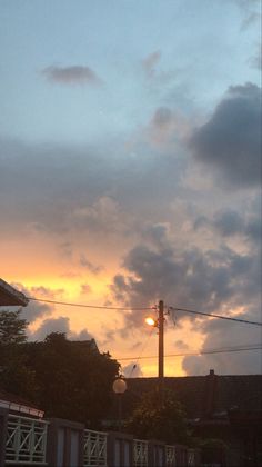 the sun is setting behind some clouds in the sky over houses and trees with power lines