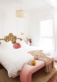 a bed with white sheets and pink pillows in a bedroom next to a large window