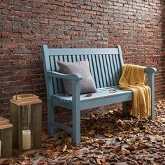 a wooden bench sitting next to a brick wall with leaves on the ground around it