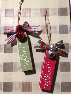 two christmas tags hanging from twine with ribbons and bells attached to each other on a checkered table cloth