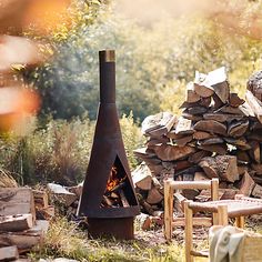 an outdoor fire place with logs stacked on the ground and a chair in front of it