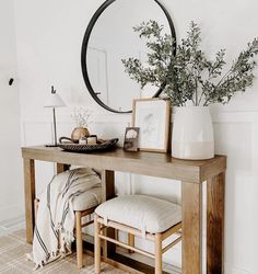 a wooden table topped with a mirror next to a white vase filled with greenery