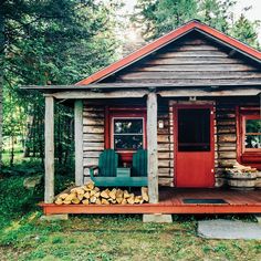 a small log cabin in the woods with a red door and green chair on the porch