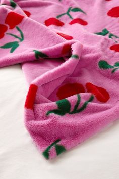 a pink blanket with cherries on it laying on top of a white bed sheet