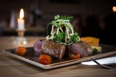 a plate topped with meat and vegetables on top of a wooden table next to a candle