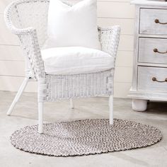 a white wicker chair sitting on top of a rug next to a wooden dresser