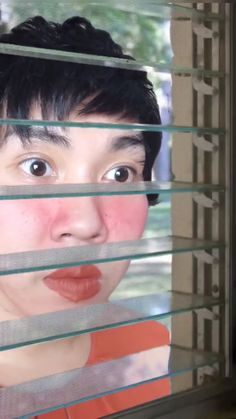 a woman looking through blinds at the camera