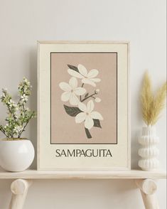 a white vase with some flowers on top of a shelf next to a framed poster