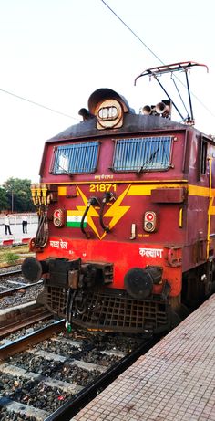 a red and yellow train traveling down train tracks next to a loading platform at a station