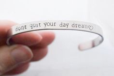 a hand holding a silver bracelet that says, don't gut your day dream