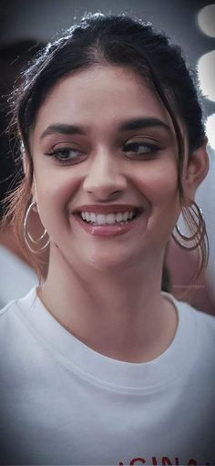 a woman smiling with big hoop earrings on her face and wearing a white t - shirt