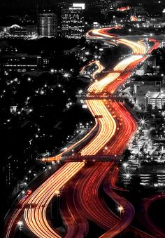 an aerial view of a city at night with light trails on the road and buildings in the background