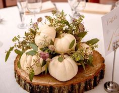 white pumpkins and greenery are placed on top of a tree slice at the head table