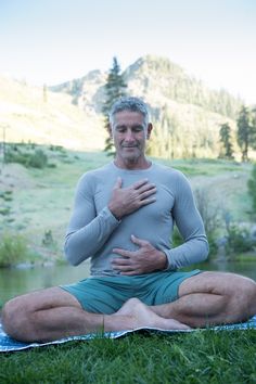 a man is sitting in the grass with his hands on his chest and holding his stomach