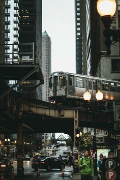 a silver train traveling over a bridge next to tall buildings on a city street at night