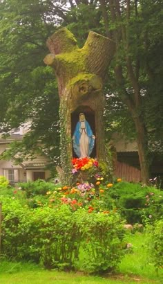 a statue of jesus in the middle of a garden with flowers and trees around it