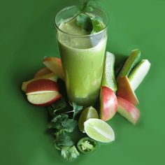 a glass filled with green liquid surrounded by sliced apples and celery on a green surface