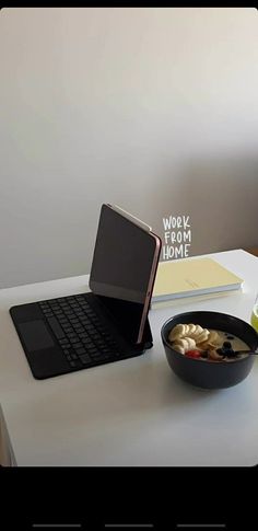 an open laptop computer sitting on top of a white desk next to a bowl of food