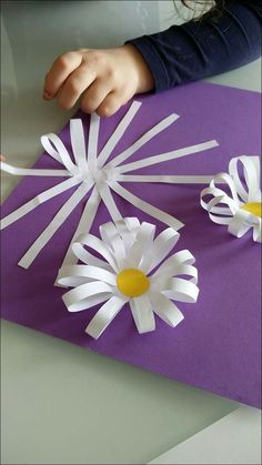 someone cutting out paper flowers with scissors on a purple tablecloth that has been folded in half