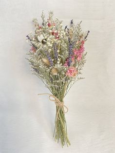 a bunch of wild flowers tied to a white wall with a brown ribbon around it