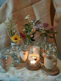 mason jars filled with flowers and lit candles on a white table cloth covered chair in the background