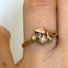 a woman's hand holding a gold ring with leaves on it and a diamond in the middle