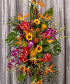 an arrangement of tropical flowers and greenery is displayed in front of a gray curtain