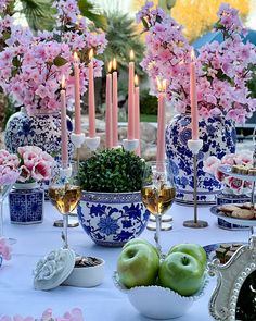 a table topped with blue and white vases filled with fruit next to candles on top of a table