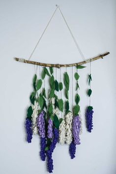 purple and white flowers are hanging from a branch with leaves on the wall next to it