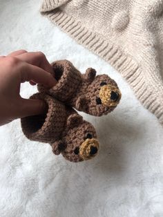 a hand is holding two small crocheted teddy bears on a white blanket next to a sweater